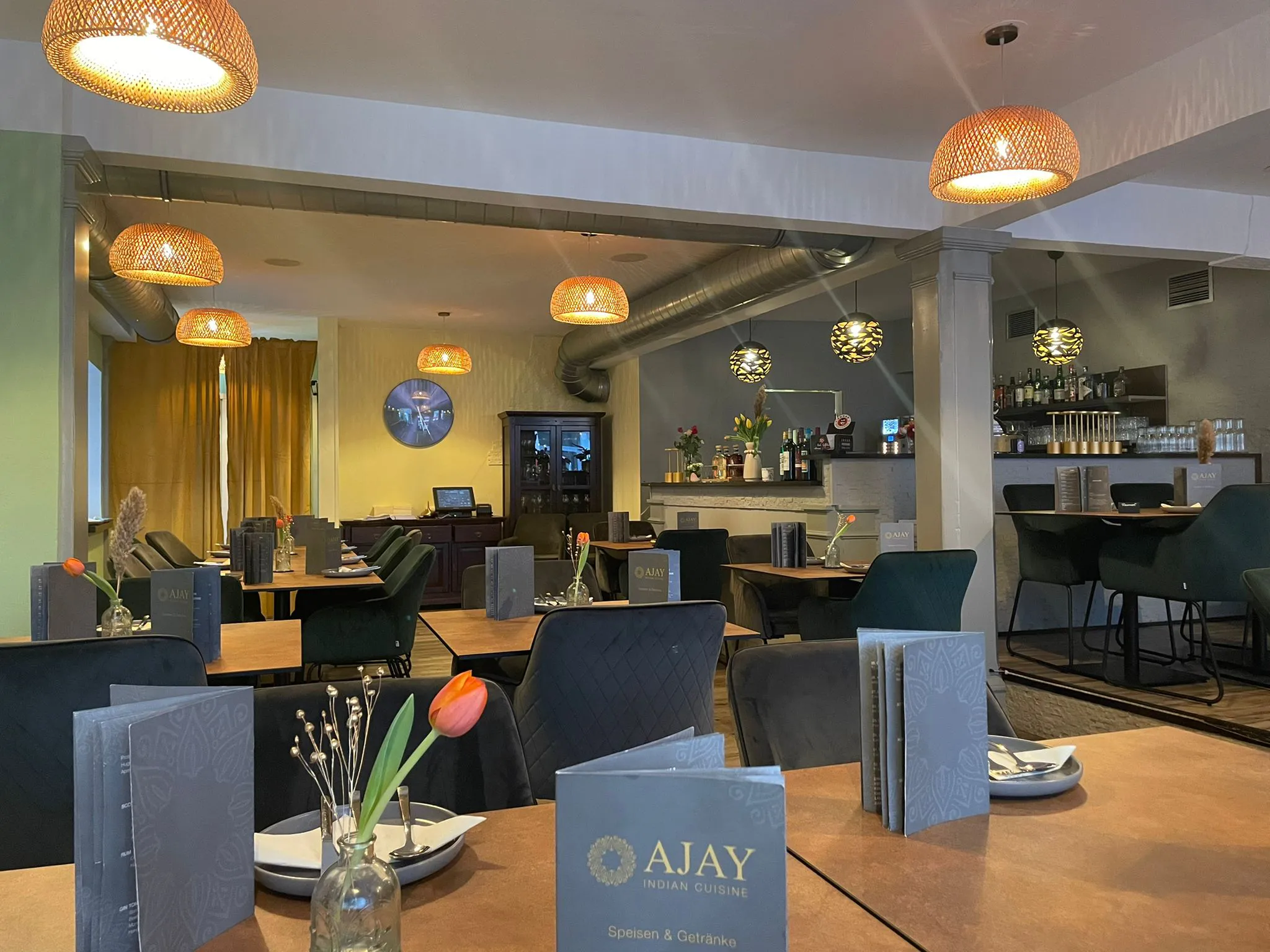 Innenansicht eines gemütlichen Restaurants mit modernen hängenden Lampen, elegant gedeckten Tischen und einer Bar im Hintergrund